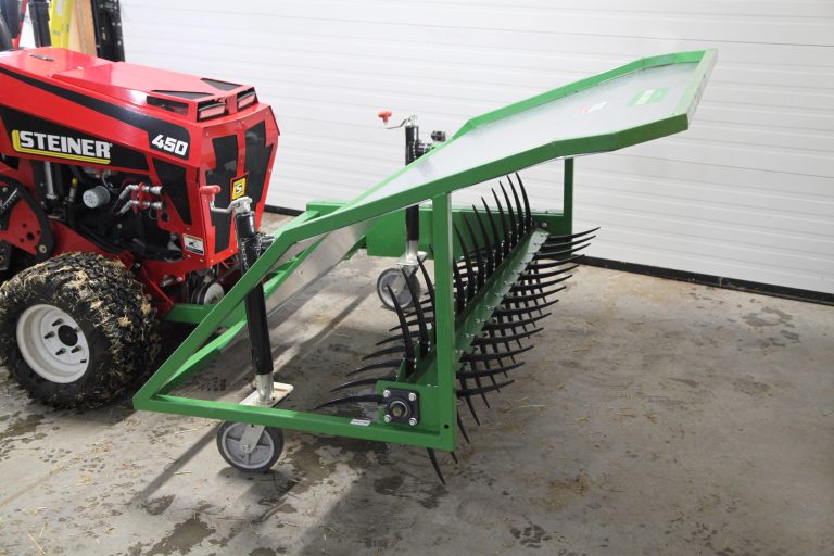 Green rotary fork attachment with curved black tines displayed beside a Steiner 450 tractor at County Line Equipment.
