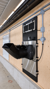 Avi-Air Avi35 Hybrid Heat Recovery Unit installed on a poultry barn wall, featuring a black ventilation duct, metal access panel and electrical controls.